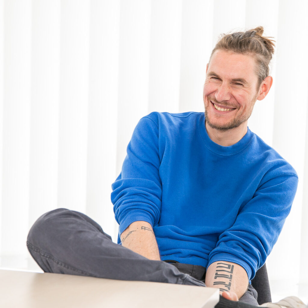 Sitzender Mann im blauen Pullover lacht